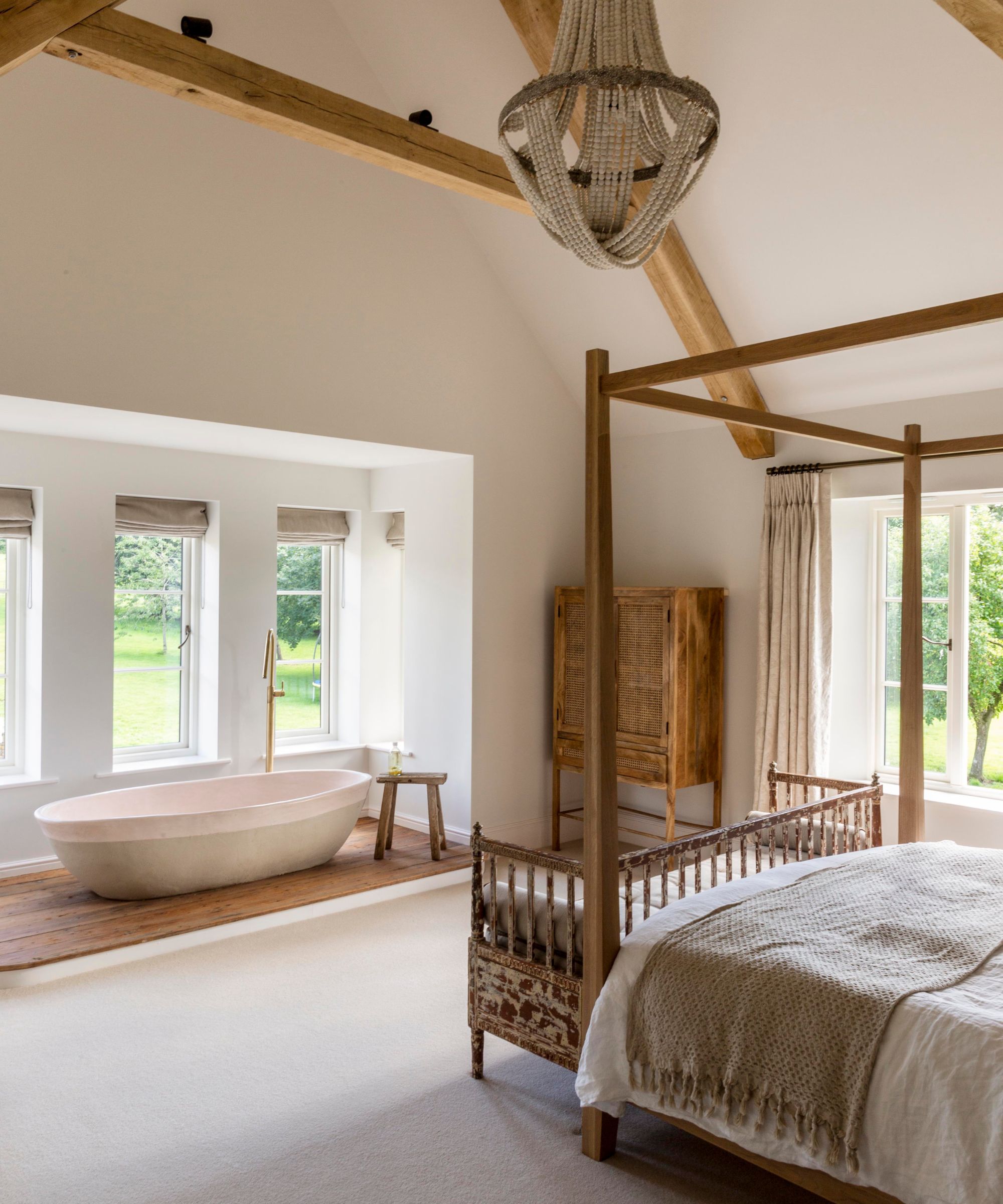 A large bedroom with a four poster bed, vaulted ceilings, and a bathtub installed by the window
