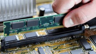 A close-up photo of a person installing a stick of RAM onto a motherboard