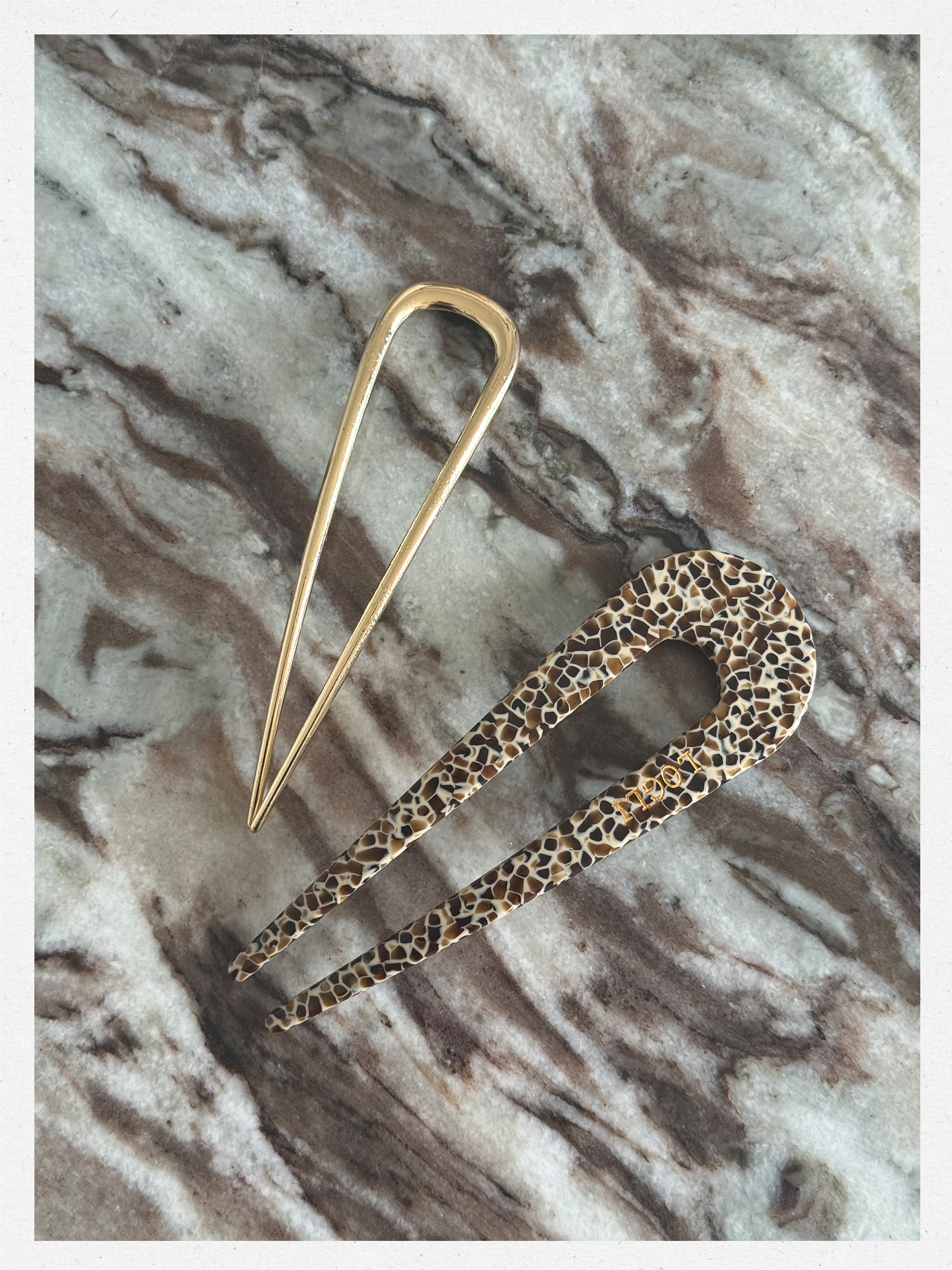 Two French hair pins on a marble table