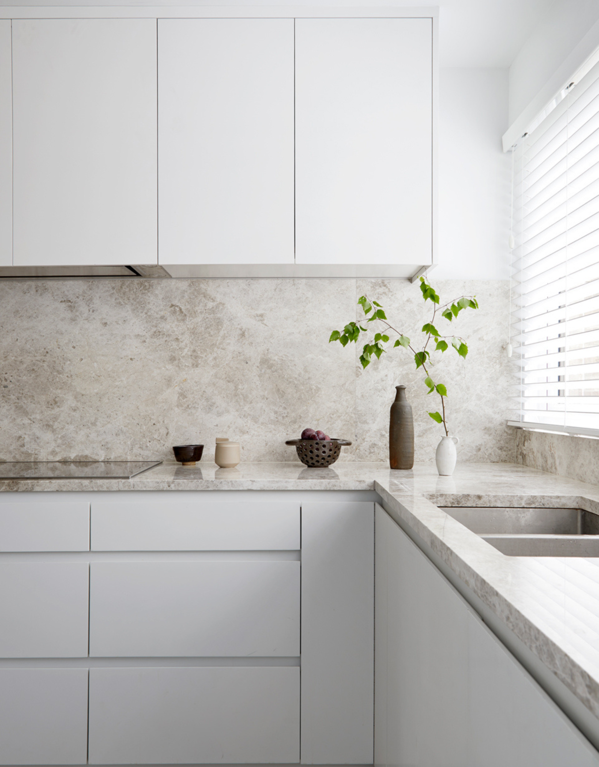 A white minimalist kitchen with seamless cabinets and a stone counter and backsplash