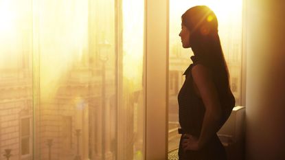 Woman looking out over the city from a high rise with the sun low in the sky.