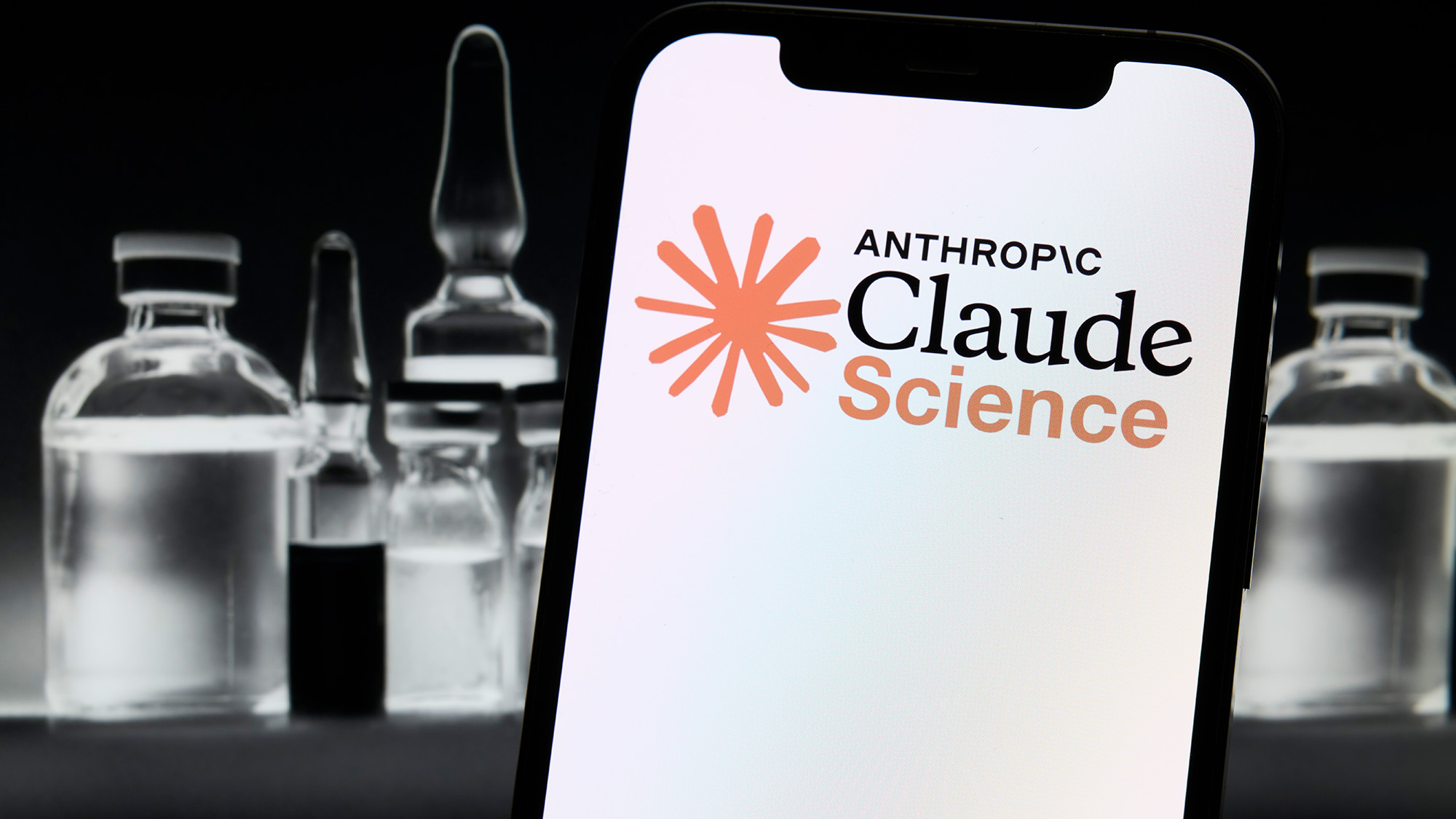 A close up of a phone with a white screen saying "Claude Science" in front of empty glass bottles