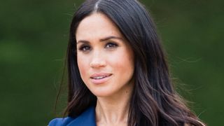 Meghan Markle wearing a navy dress, with a serious expression on her face