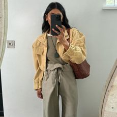 Monikh wearing a clay green top and pant set with a cropped yellow jacket and woven brown shoulder bag. 