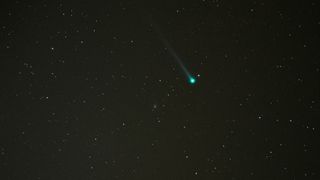 A greenish comet streaks through the night sky.