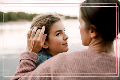 Mum stroking hair of young teenage daughter as they walk by a river 