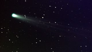 A green comet seen streaking through the night sky with an icy tail dragging behind it