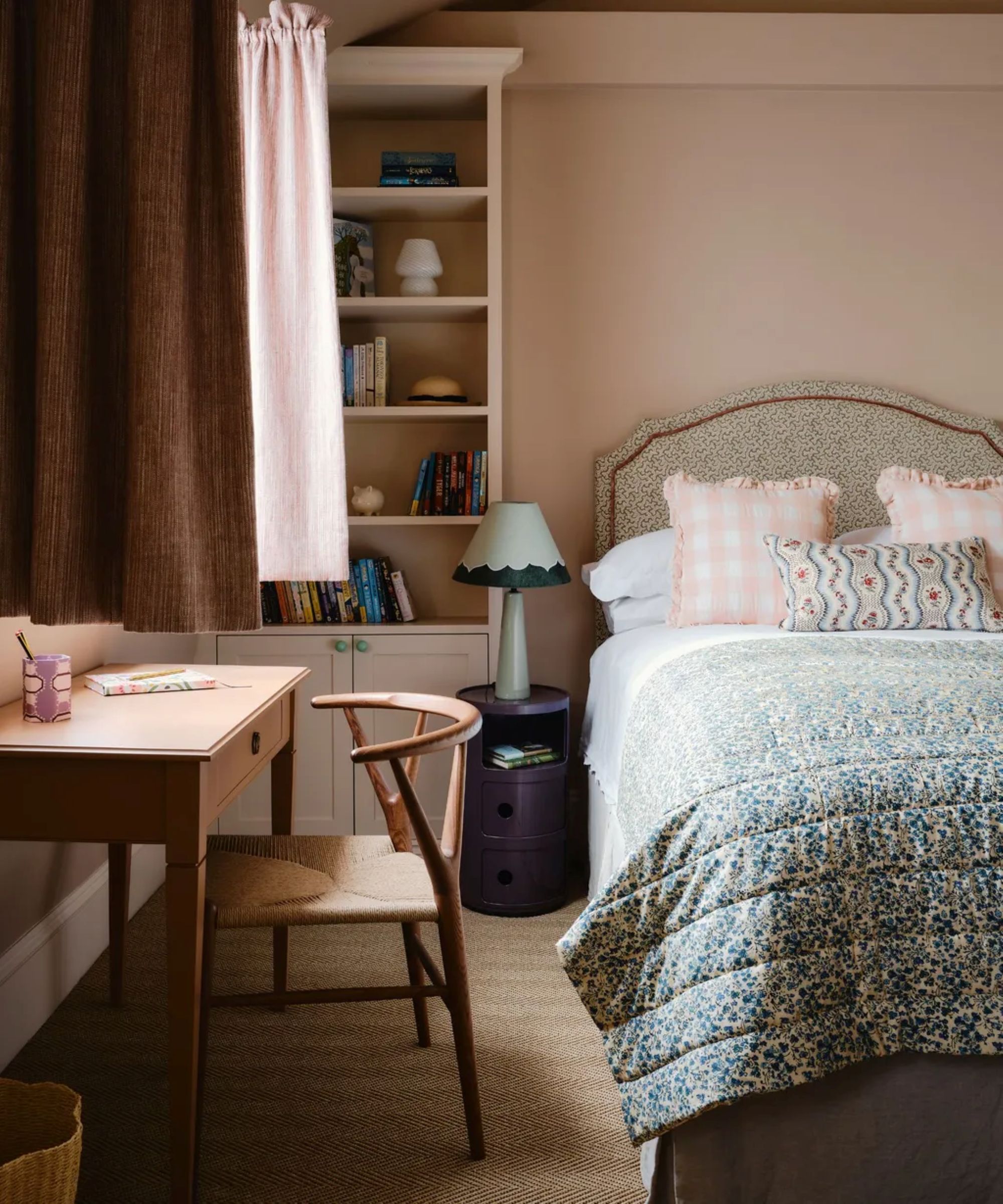 a bedroom with a small desk, a chair, a twin side bed with floral bedding, and a bookcase in the left corner