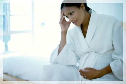 A pregnant woman in a dressing gown touches her baby bump and looks worried about bleeding during pregnancy
