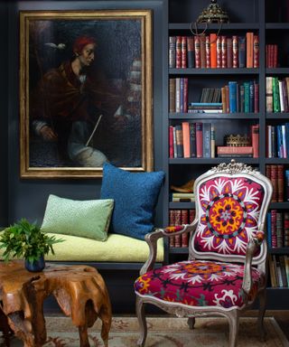 dark library corner with patterned armchair, bright colored cushions, vintage artwork and bookshelves