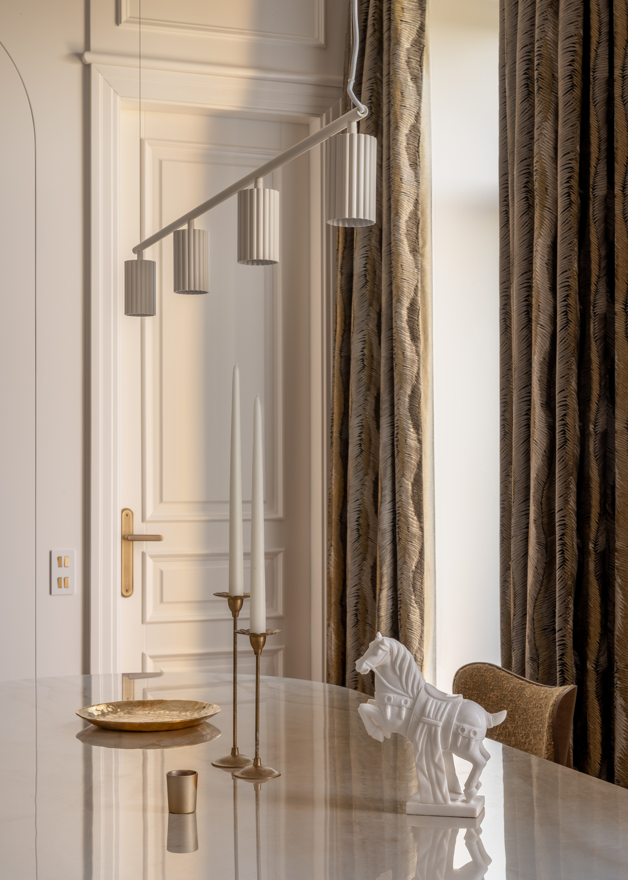 A marble table with white tapered candles and gold candlesticks by a gold mini cup, and a gilded plate