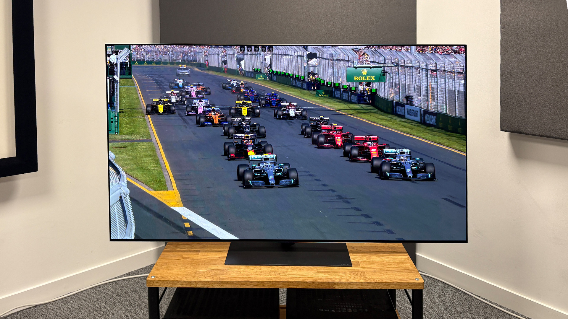 The 65-inch LG G5 OLED TV pictured on a wooden rack. On the screen is a still from Netflix F1 series Drive to Survive.