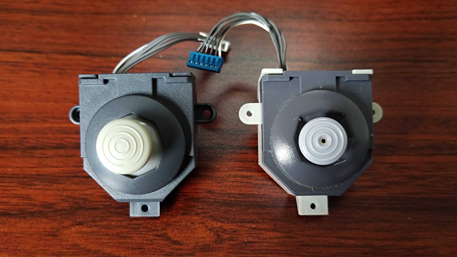 Hyperkin N64 thumbstick next to original on woodgrain desk.
