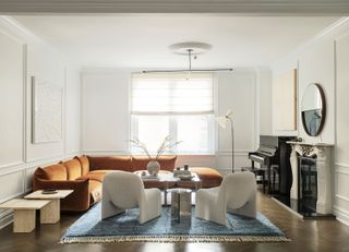 white living room with orange l shaped sofa and two modern accent chairs