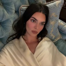 Kendall jenner lays down wearing a silk ivory top.