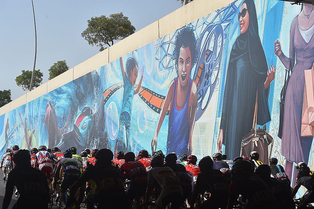 The peloton passes a mural Abu Dhabi Tour