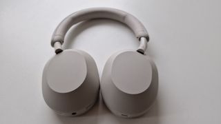 Et par hvide Sony WH-1000XM5 ligger fladt på et hvidt bord.