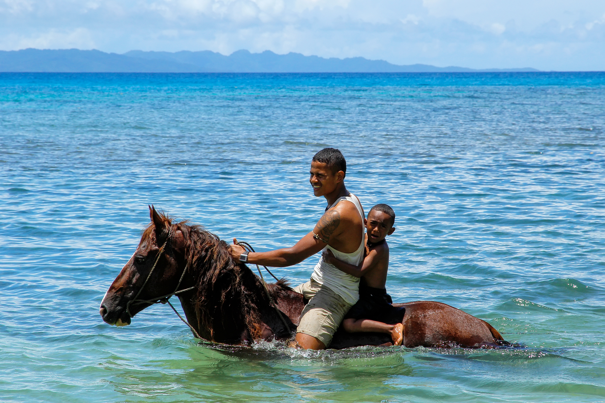Young man with a boy riding horse on the beach on Taveuni Island, Fiji. Taveuni is the third largest island in Fiji.