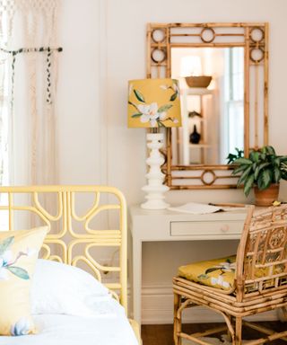 A bedroom with a wicker chair, light yellow bedframe, and wicker mirror