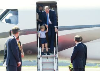 Prince William and toddler Prince George walking down the stairs of a plane, both wearing navy blue outfits