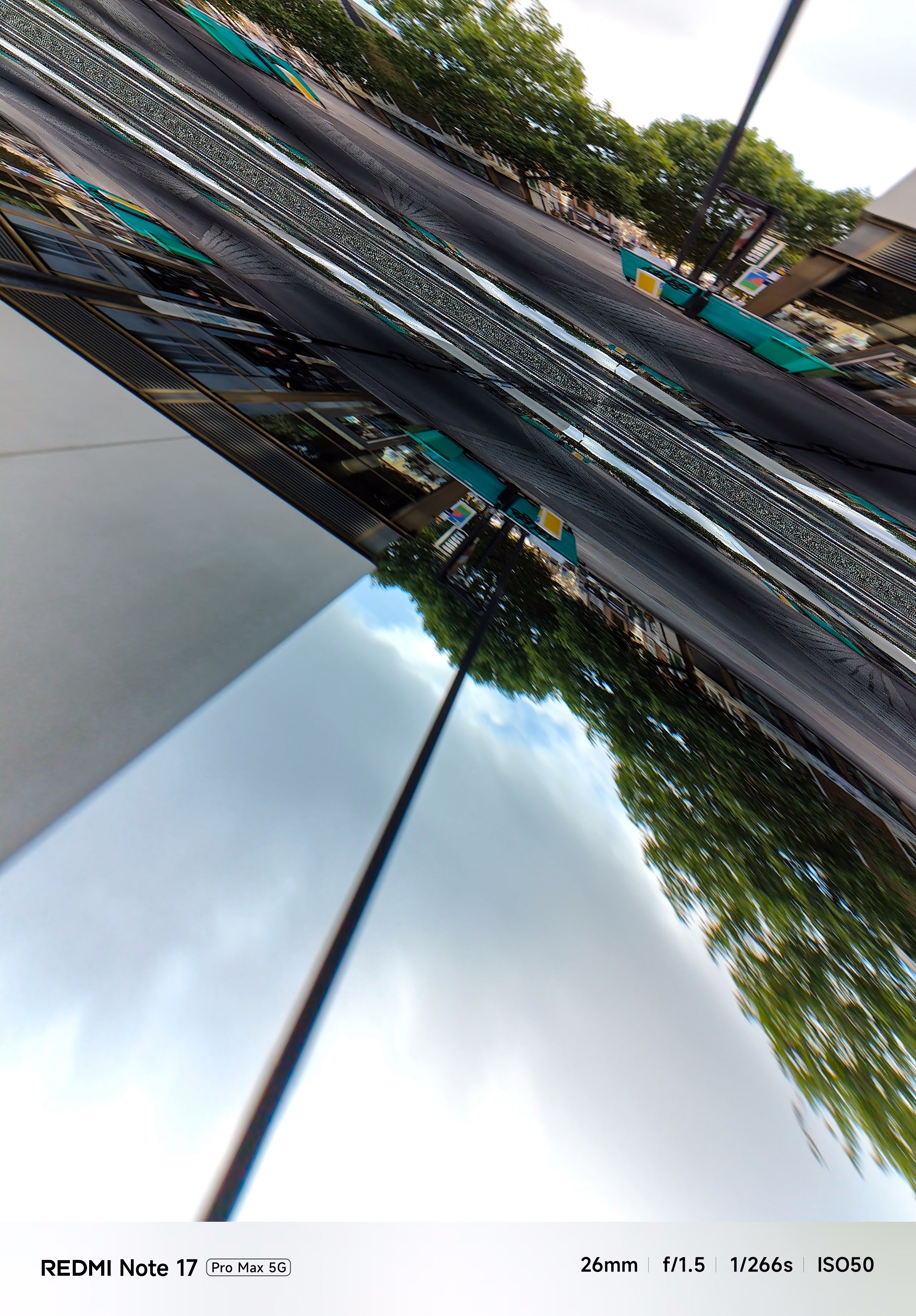 Severely distorted camera image showing mirrored and stretched reflections of a modern pedestrian area.