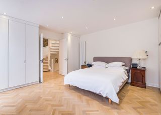bedroom with white wall and light parquet flooring and grey bed