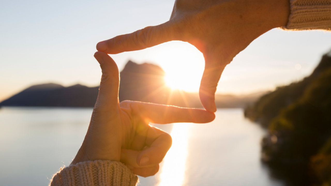 A pair of hands frame the sun between them.