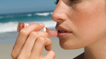 woman putting on lip balm on a beach
