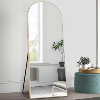 gold-rimmed floor length mirror leaning on a stand with minimalistic decor