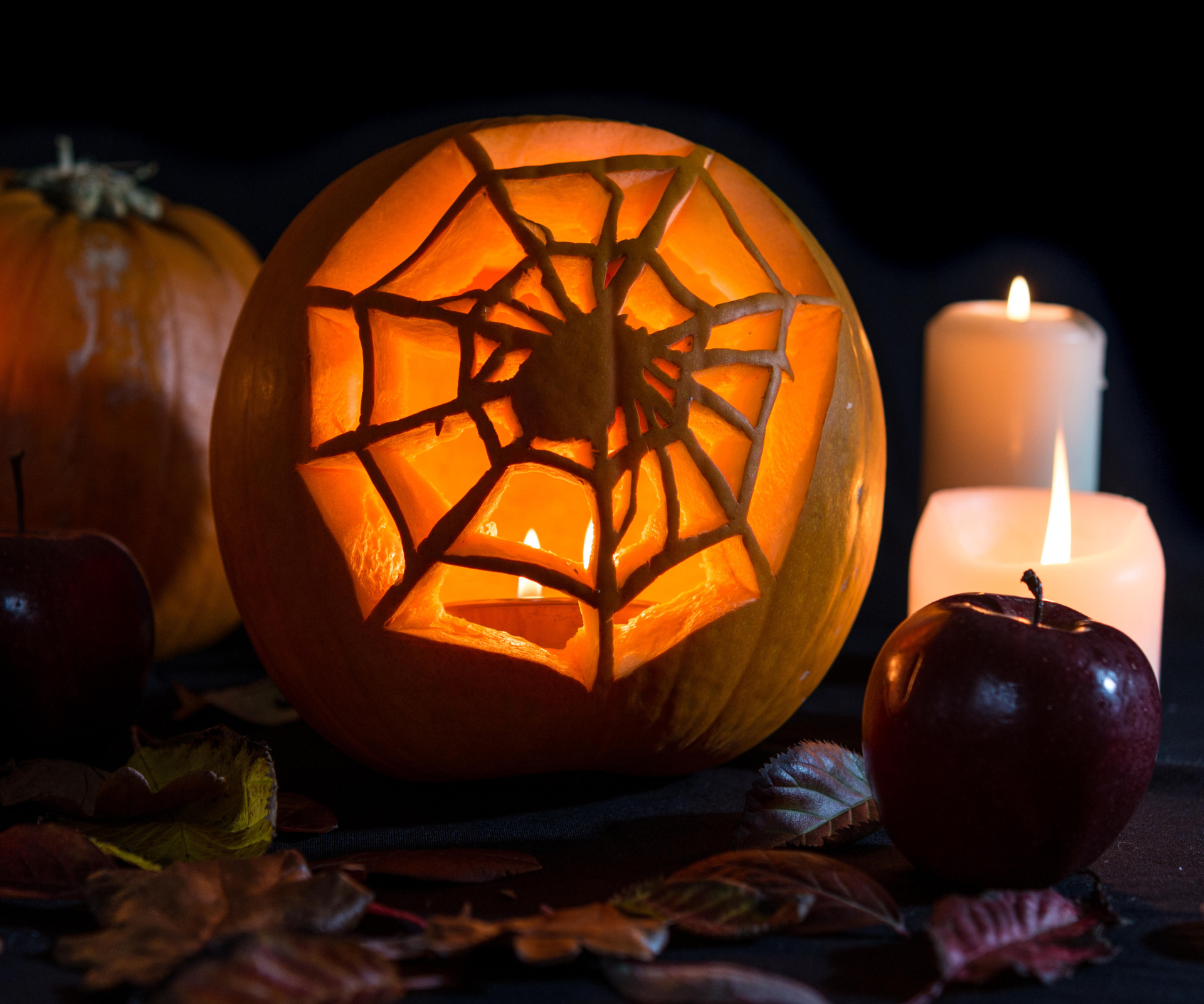 Spider & web carved pumpkin with apples and candles