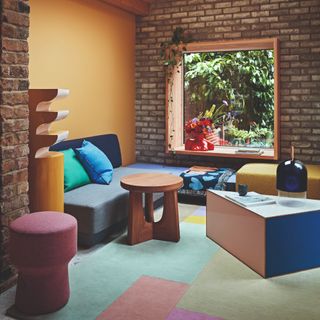 A living room with a mustard yellow wall and colour-blocked rug with colourful furniture