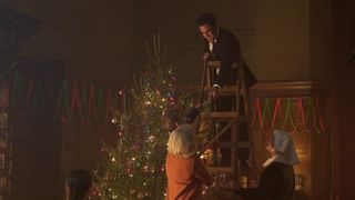 Olly Rix in a suit as Matthew stands on a ladder decorating a Christmas tree as Trixie (Helen George), Jonty (Archie O'Callaghan), Sister Veronica (Rebecca Gethings) and Nancy (Megan Cusack) look on in Call the Midwife.