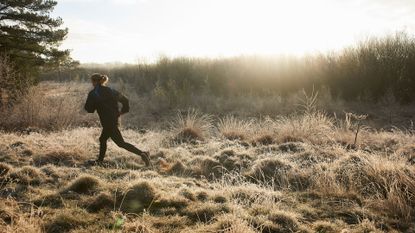 Woman running through park in the winter, showing what to wear running in the cold, sun setting in the distance and frost on grass