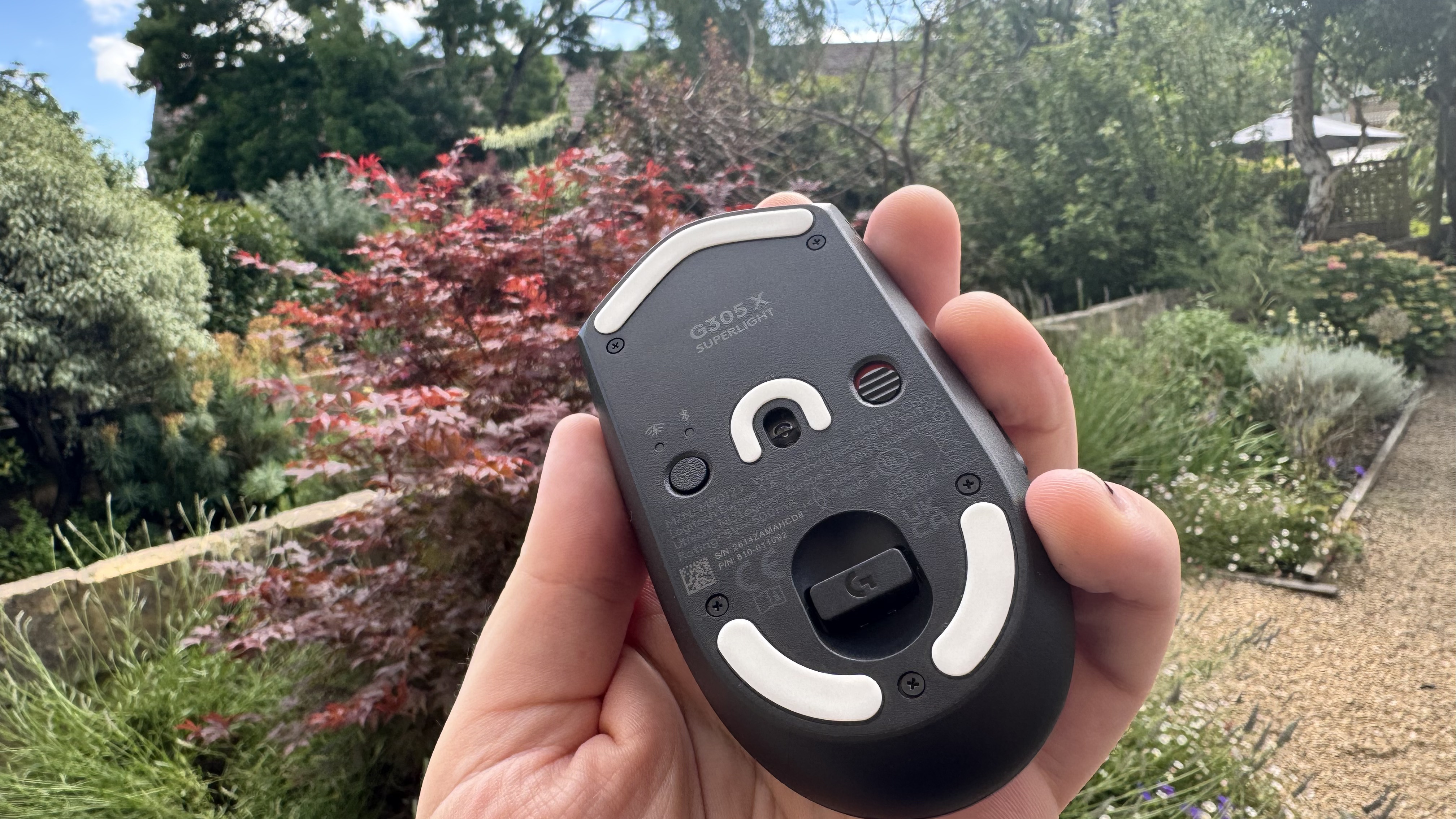 Logitech G305 X Superlight gaming mouse, held in a hand outside