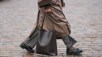 A close up shot of a woman walking down the street carrying a chic bacl work bag - 1975353224