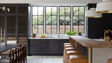 Kitchen with large windows, dark cabinets, wood island and leather seat stools