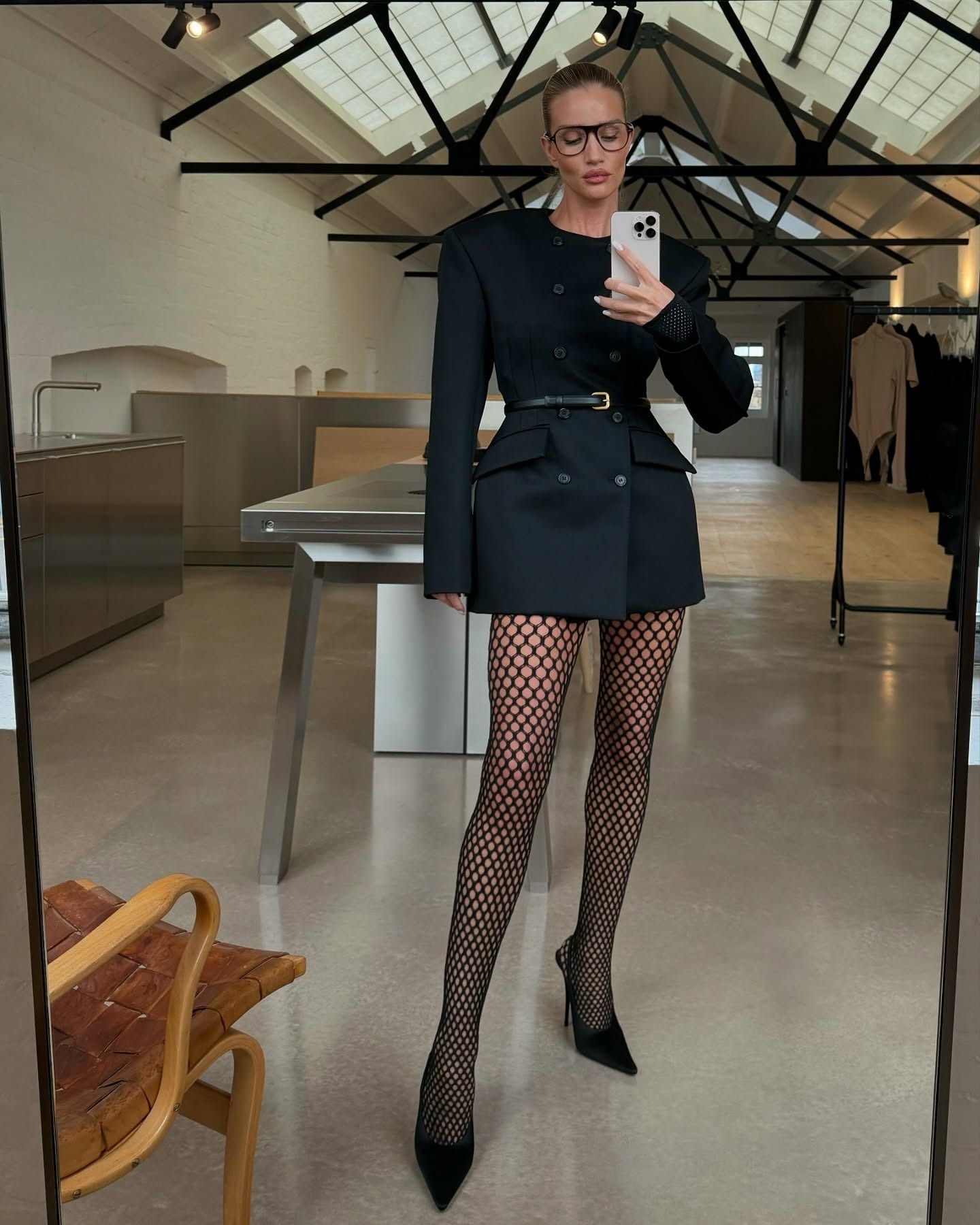 Rosie Huntington-Whiteley takes a mirror selfie wearing a her black Wardrobe NYC blazer dress with fishnet tights and black pointed-toe heels.