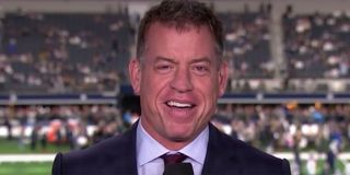Troy Aikman talking into a microphone on an NFL broadcast.