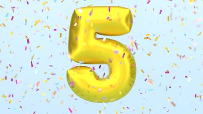 A gold party balloon in the shape of the number five surrounded by confetti.
