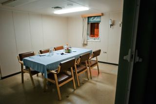 A modest dining table set for a meal inside a room on a container ship/