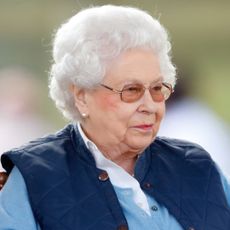 Queen Elizabeth wearing a blue vest and glasses and smirking