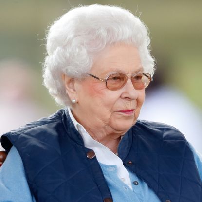 Queen Elizabeth wearing a blue vest and glasses and smirking