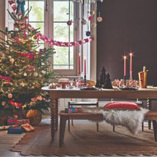 A purple-painted dining room with a decorated Christmas tree in the corner and a set dining table with matching benches