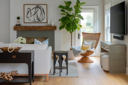 living room with rattan chair, fig tree, stripe console, tv, white couch, rug, fireplace, artwork