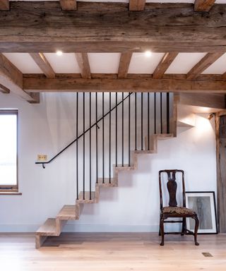 room with wooden beamed ceiling, wooden floor and cantilevered wooden staircase with black metal stair rods