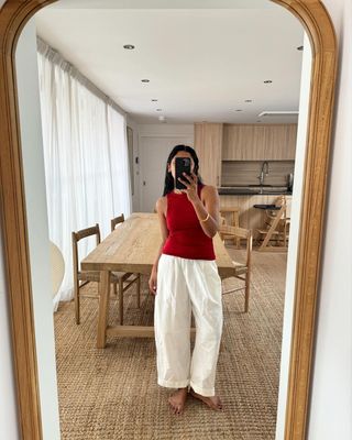 @monikh wearing red tank, white poplin pants, taking picture in a mirror