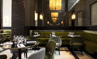 Monsieur Bleu, Paris, France. A restaurant with green "L" shaped seating booths with tables and chairs around them, a large wall mirror, wall lights and large square yellow pendant lights above.