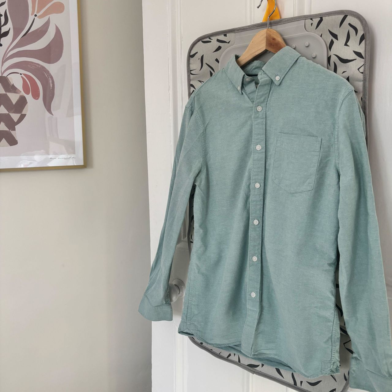 steamed green shirt hanging on a door with artwork on the wall