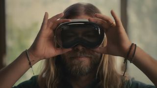 A screenshot from the promotional video for the Apple Vision Pro headset, showing a long haired man holding on to a pair like Dambuster goggles