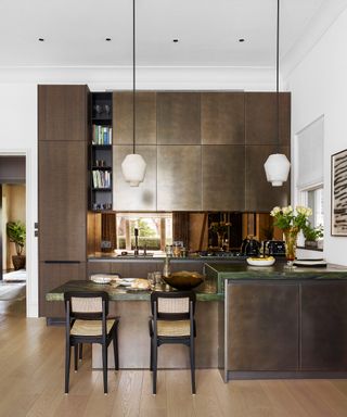 A kitchen lighting idea with downlighters and pendants hung from double height ceiling over brown cabinetry